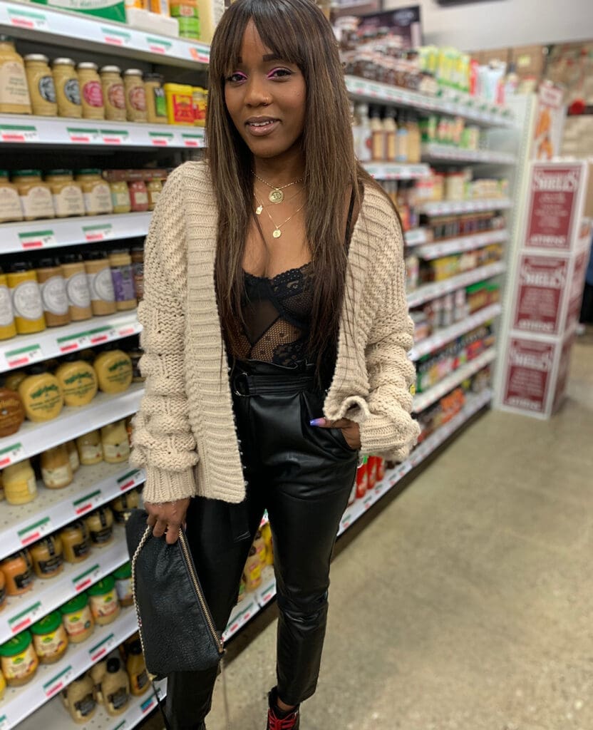 Woman poses in stylish black outfit in grocery store isle.