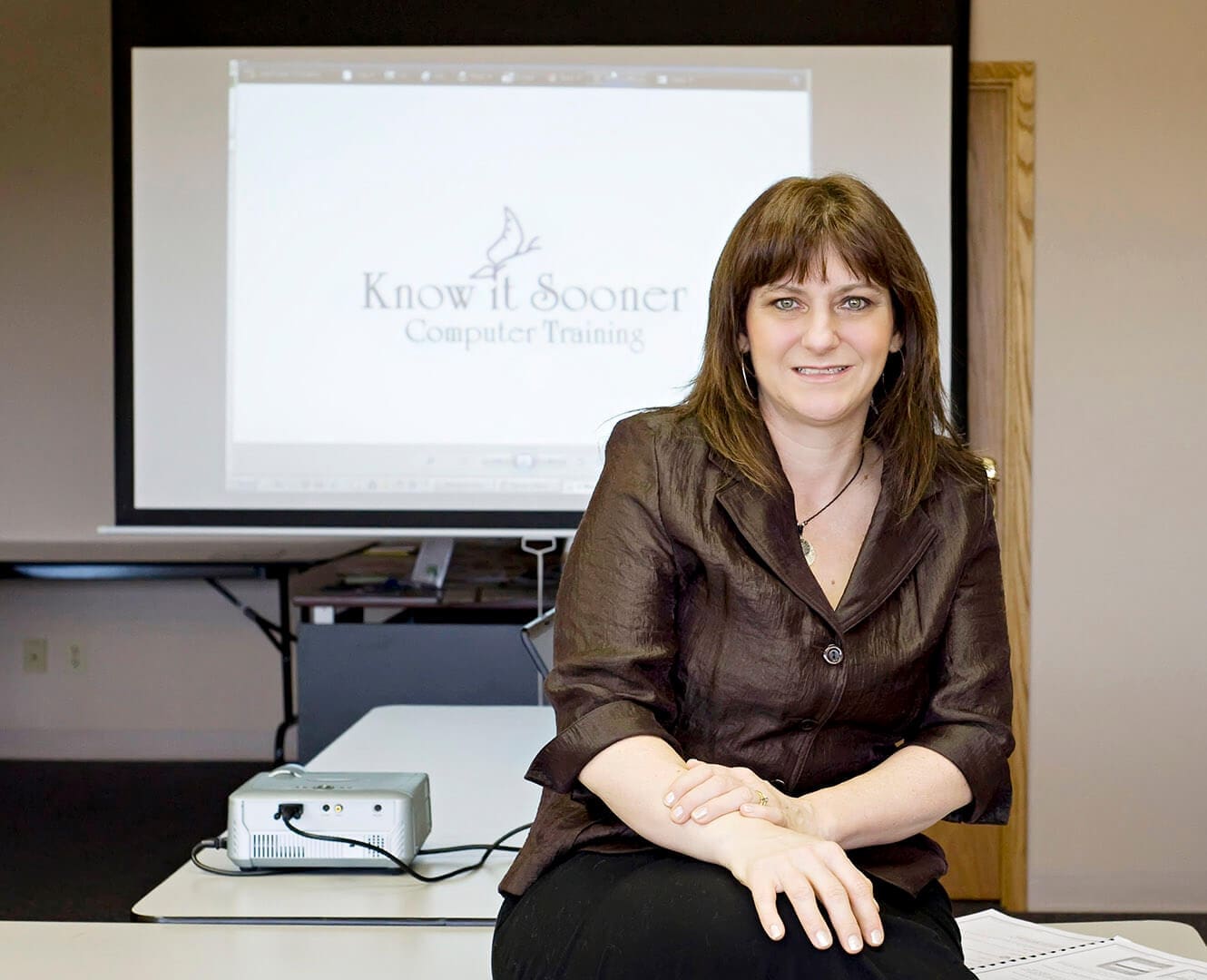 Woman sits on desk in front of slideshow on display
