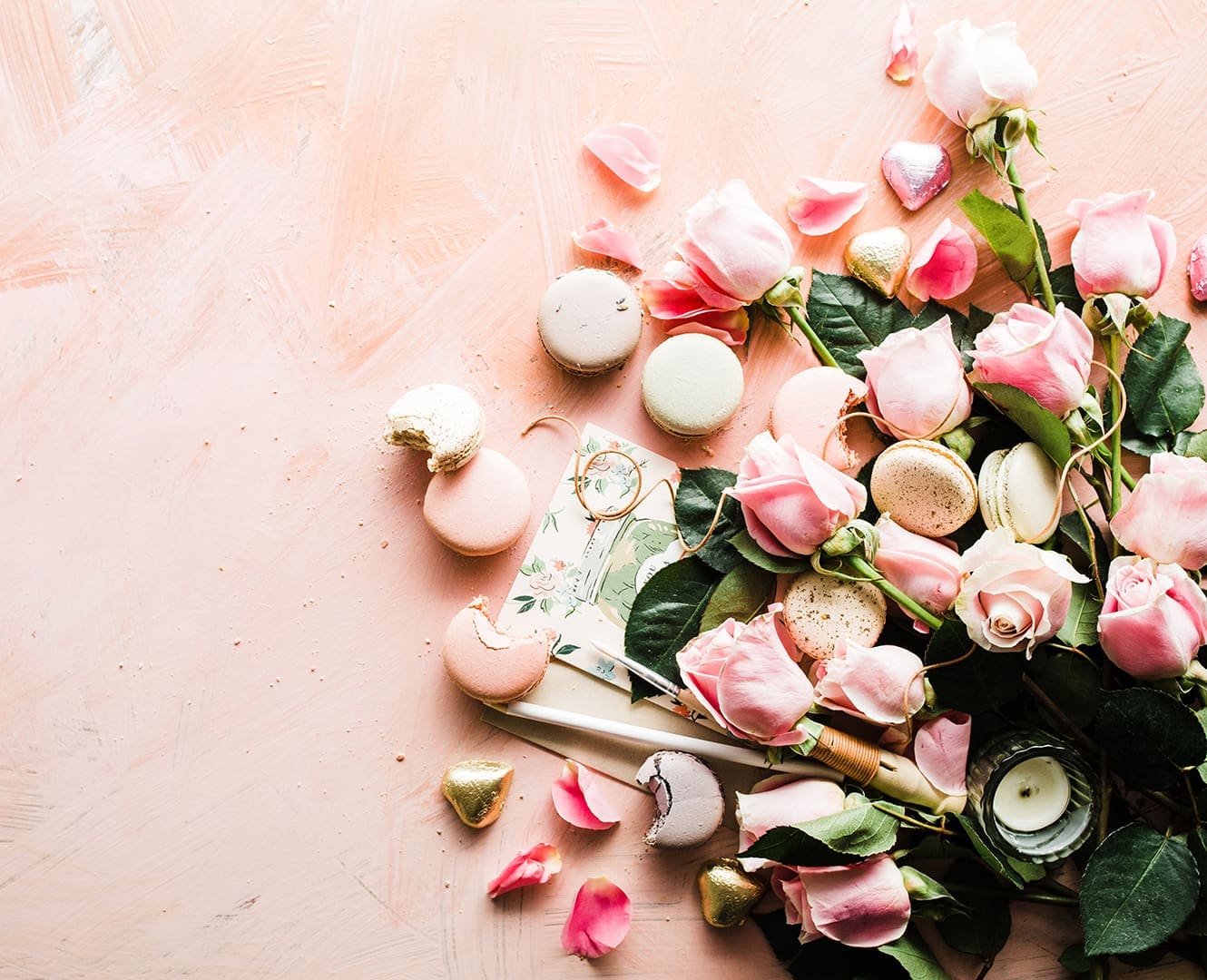 Roses macaroons and chocolates spread out on white surface