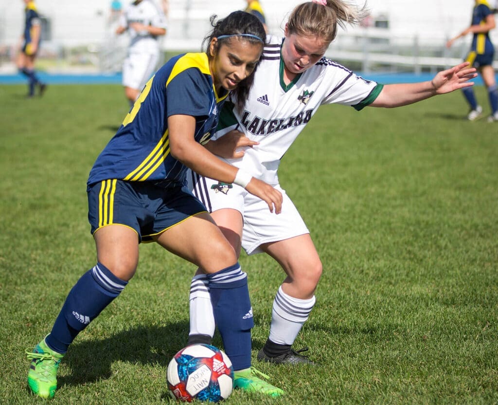Woman battling for soccer ball on soccer field in summer