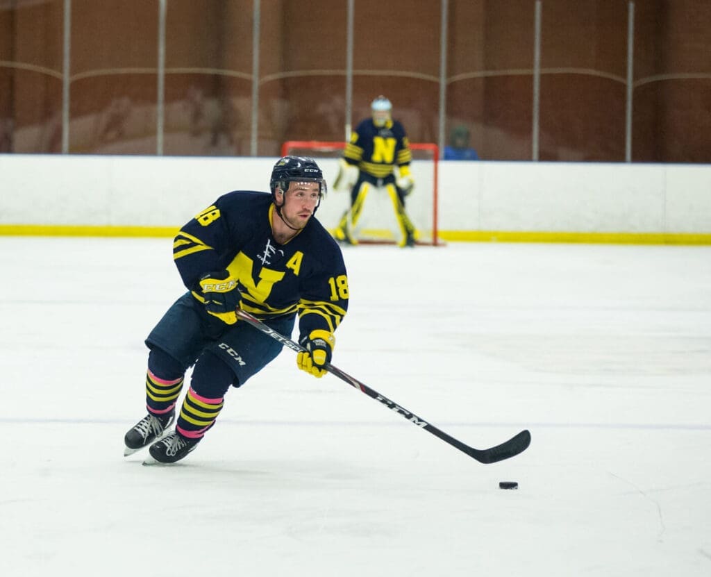 Male hockey player skates down centre of arena with puck on stick