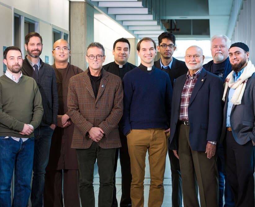 group of chaplains stand in hallway at NAIT smile for camera