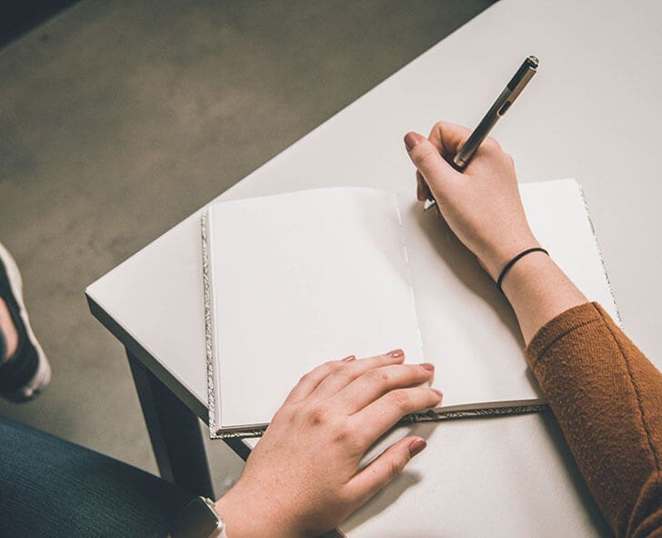 Woman sits at a table with empty notebook writing