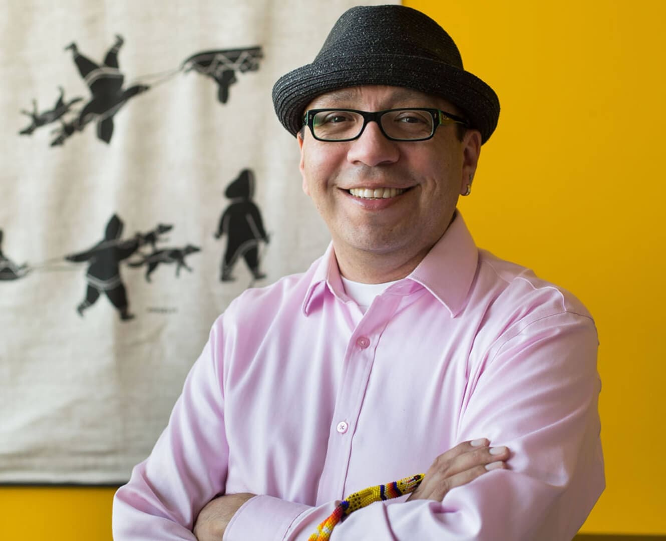 Aboriginal man stands wearing fedora hat against yellow backdrop