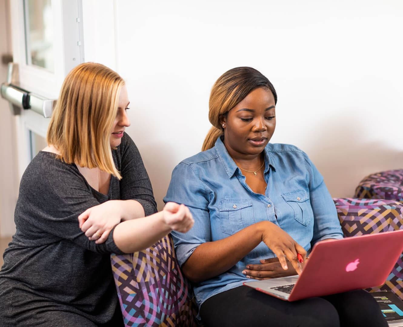 Two women sit on couch working on a laptop