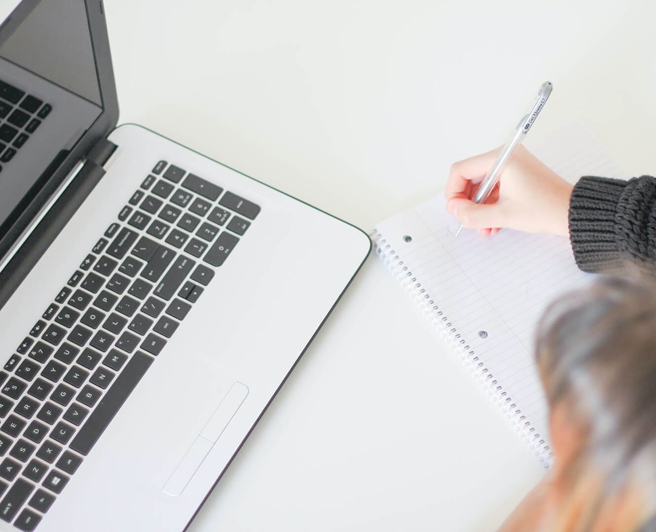 Person writing on notepad with laptop open in front of them