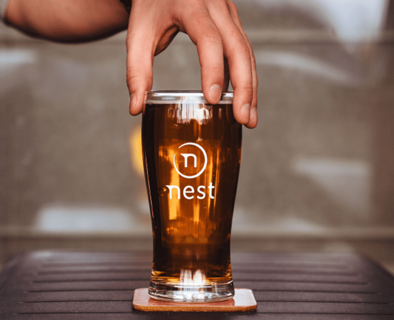 a hand holding a glass of beer with the logo of the nest on the from of the glass
