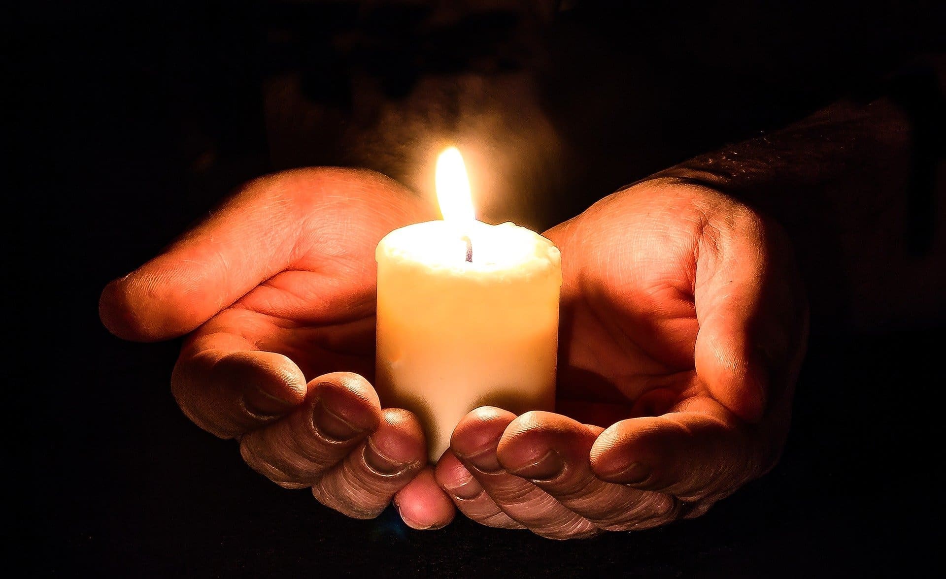 hands cupping a small lit candle. the background is dark.