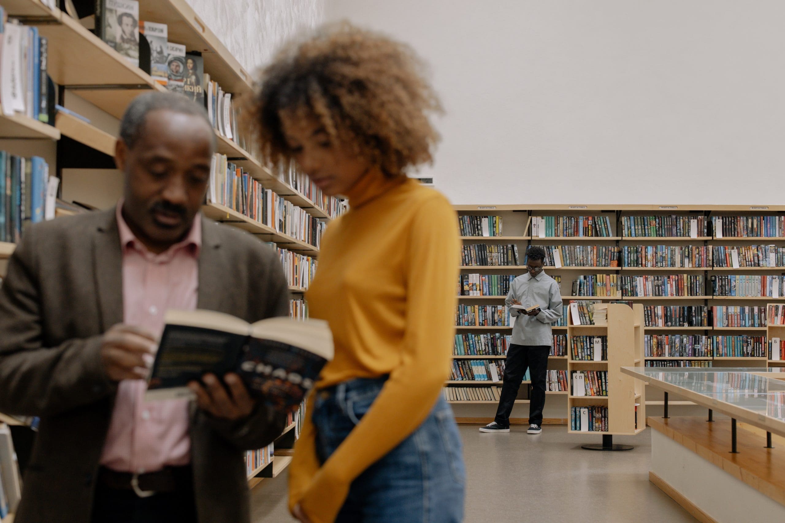 old and young read book in library Older black man and younger black woman read a book in a library. They are slightly out of focus.