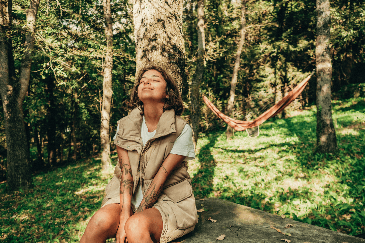 a woman sitting outside in nature. she is taking a deep breath.