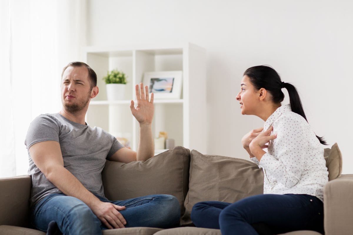 a man in a grey shirt and a woman in a white shirt are arguing. the man has his hand up and looks away. the woman is pointing at herself and is shouting.