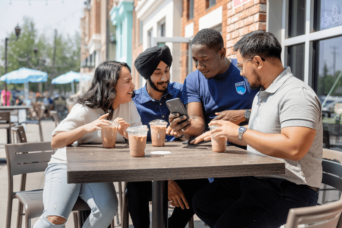 mental health A group of students sitting with iced coffees at a table. They are laughing and looking happy.