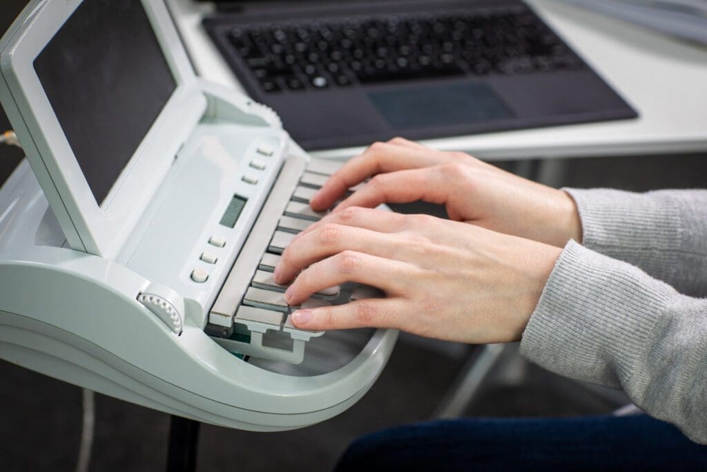 A pair of white hands type on a stenography machine.