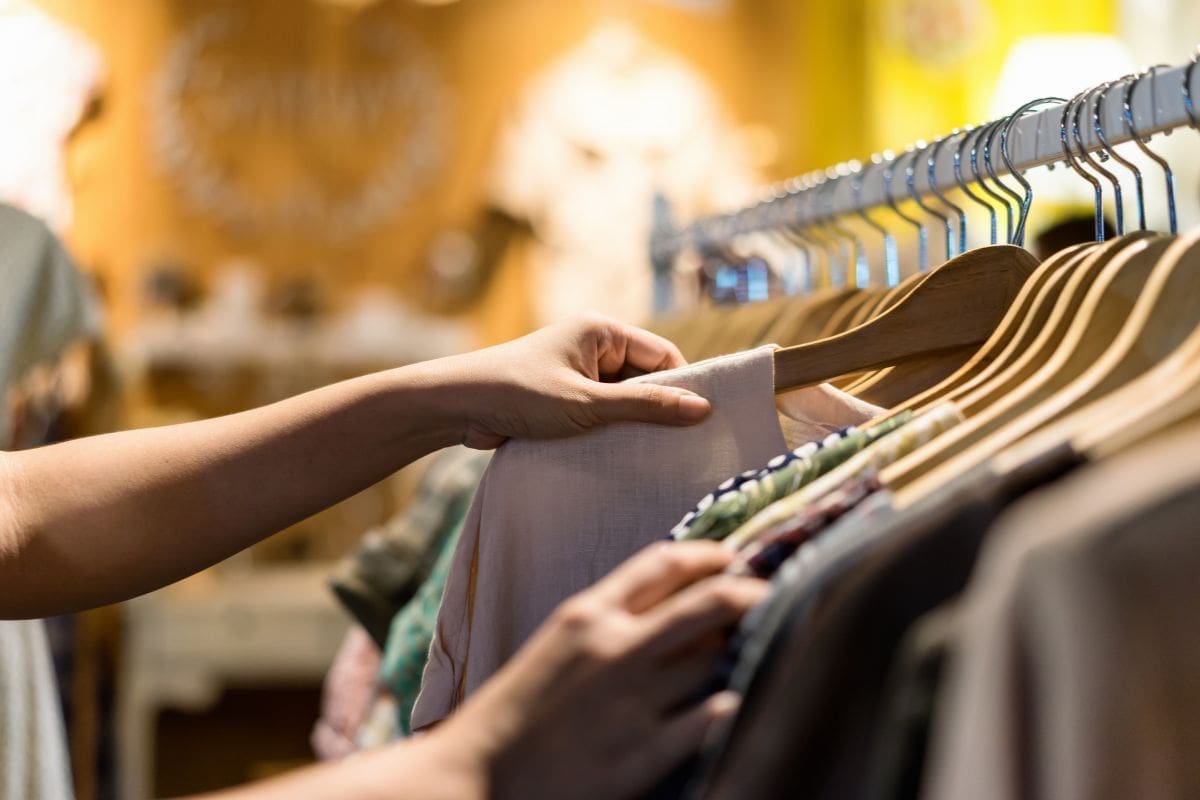 Hands hold a shirt on a hanger out from the rack to examine it.