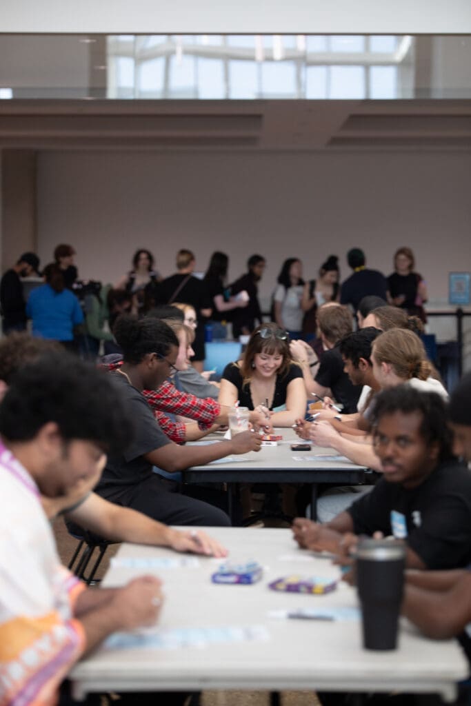 Students sit at tables, playing games and talking amongst each other. 
