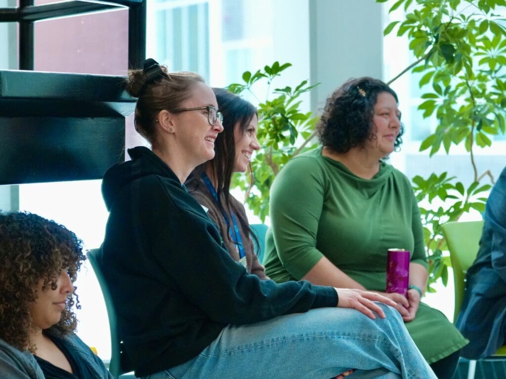 Three women watch something ahead with smiles on their faces.
