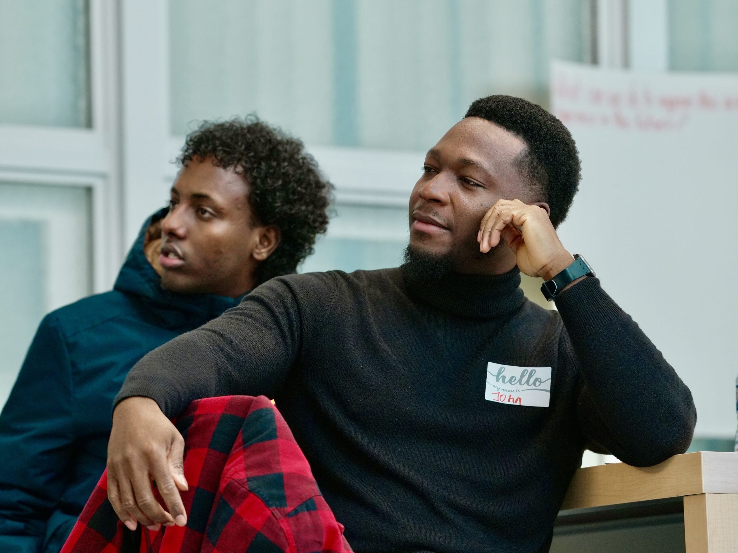 Two young Black men stare ahead, watching the speakers, with thoughtful expressions on their faces.