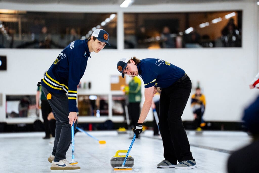 Two male curlers sweep a rock down the ice. 