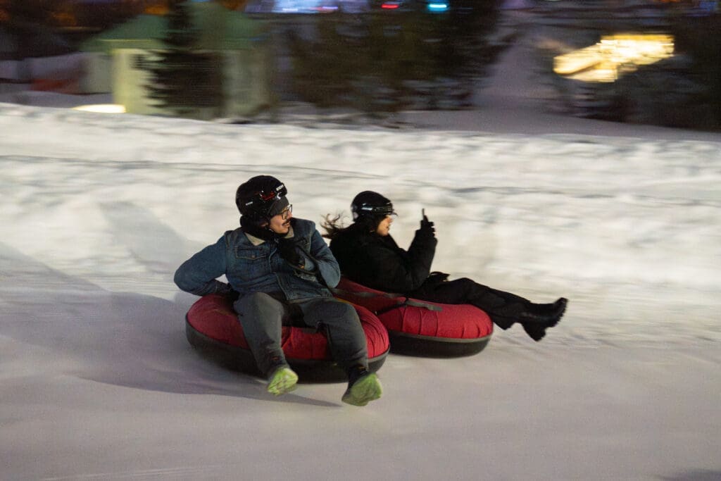 two students sitting in tubes slide down a ski hill