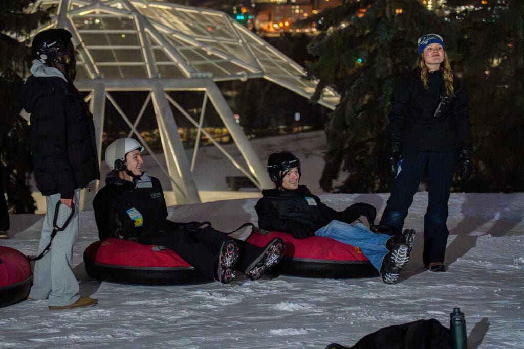A group of young people sit in snow tubes at the top of a ski hill.