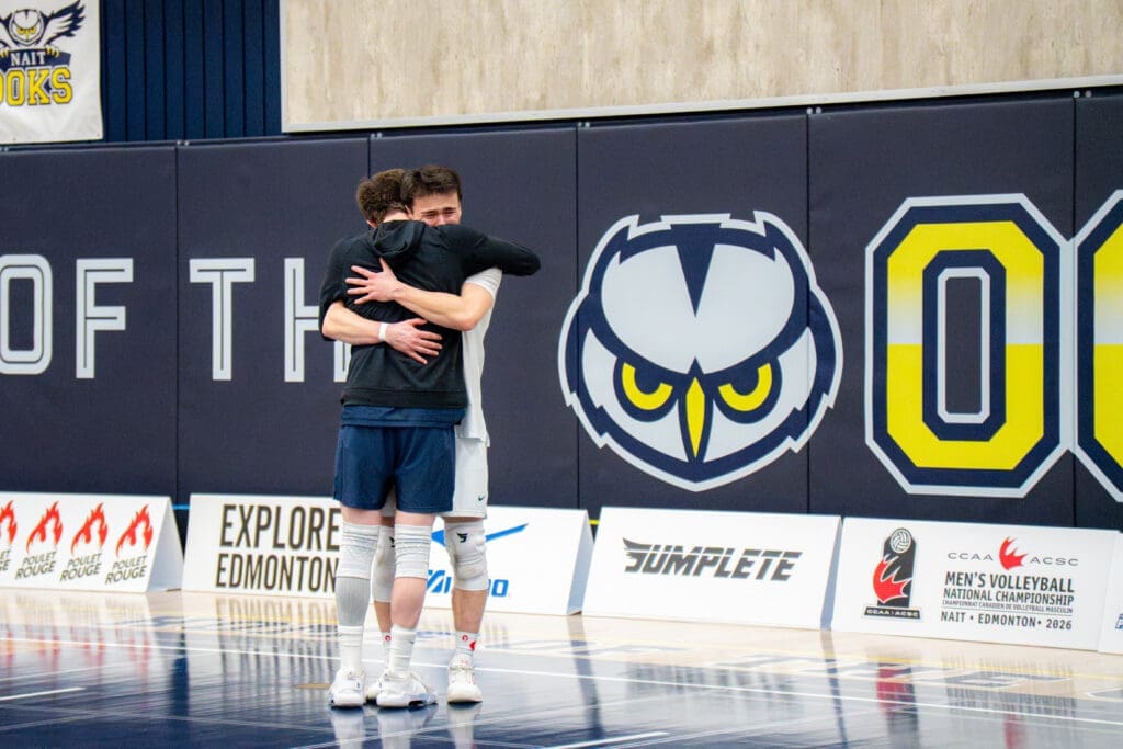 Two men in athletic gear embrace. One has his back to the camera, the other looks visibly distressed and emotional. 