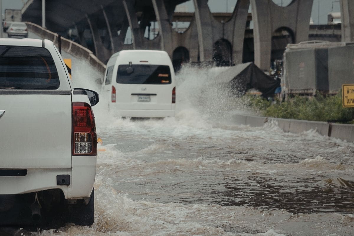A white car and truck drive through a flooded street.