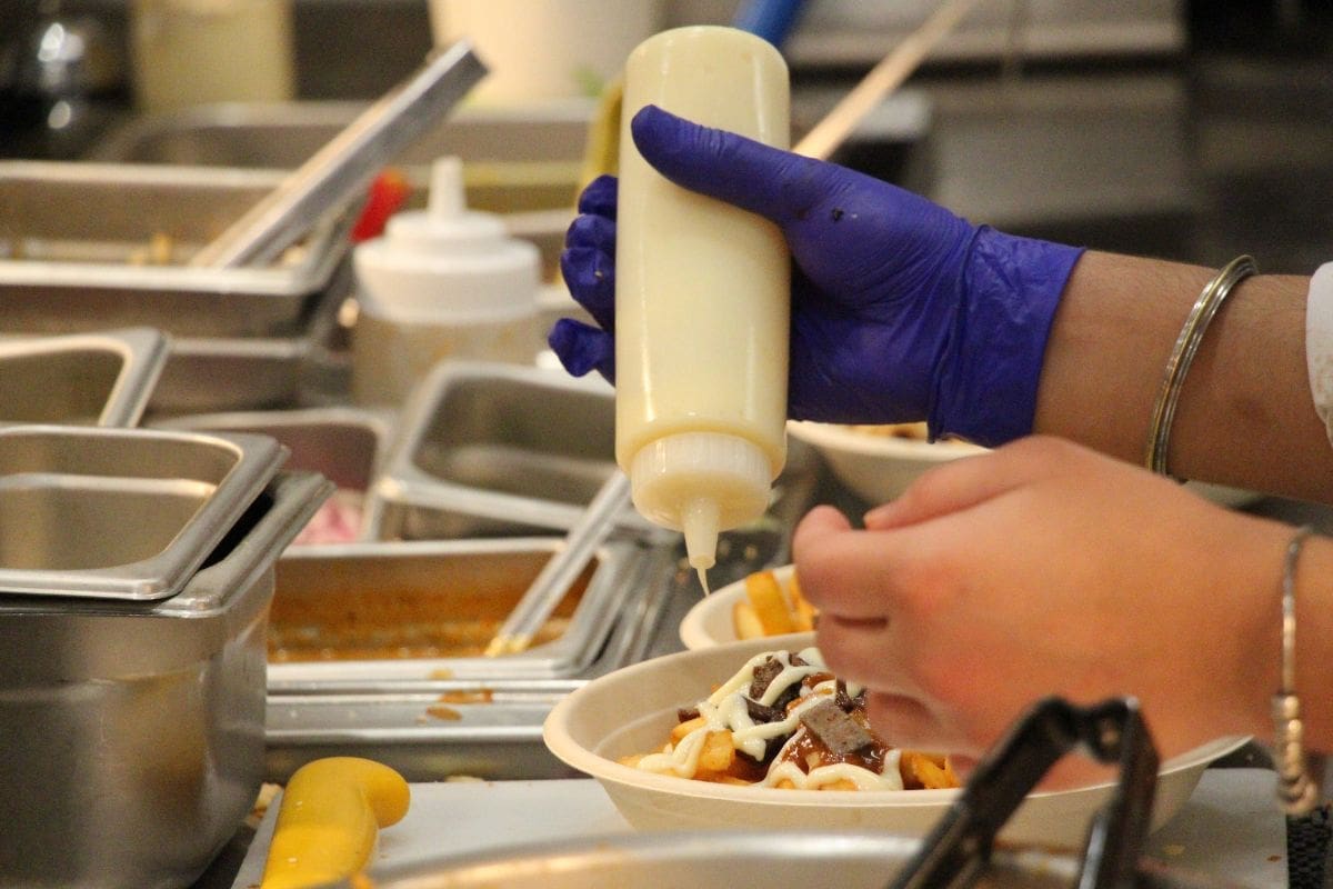 a gloved hand squeezes a bottle of sauce onto a bowl of food